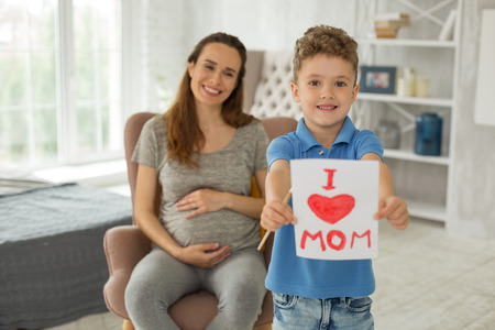 Loving son. Loving little smart son feeling very entertained while painting picture showing big love for his pregnant motherの写真素材