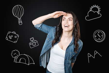 Leisure time. Cheerful young tourist feeling good and smiling while putting her hand to the head and looking into the distanceの写真素材