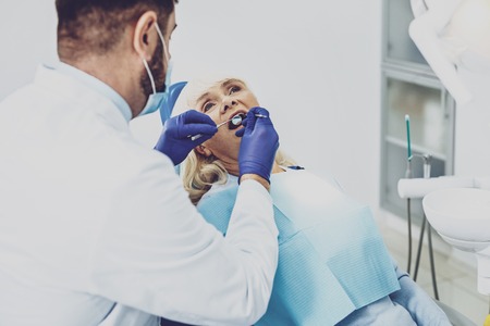 Good quality. Attentive male person using medical instrument while treating mature patientの写真素材