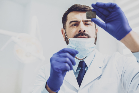 Let me check. Serious dentist raising left hand while being at his workplaceの写真素材