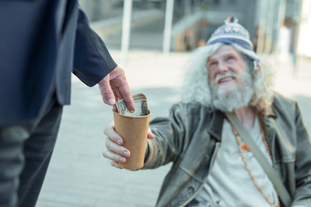 Dollar bill. Businessman wearing nice dark suit giving one dollar bill to poor street musician smiling kindly to himの写真素材