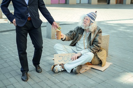 Homeless non-conformist. Homeless non-conformist feeling lost and distracted while begging for job sitting on the floor outsideの写真素材