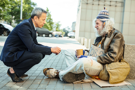 Ask for help. Helpful office worker asking starving street person sitting on the floor outside about needed foodの写真素材
