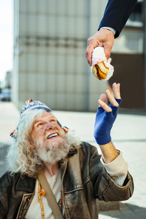 That burger. Homeless man wearing old leather jacket taking burger from kind stranger aiming for helping himの写真素材
