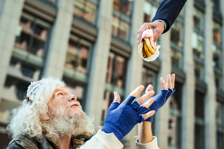 Begging for food. Hopeless street person feeling lost while begging for some food sitting near fancy office centerの写真素材