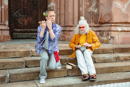 Street musicians. Street musicians wearing bright bizarre clothes and glasses playing music sitting...