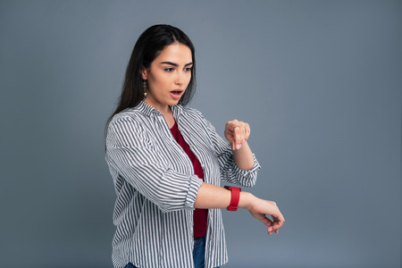 Too late. Dark-haired young woman looking at her watch and learning that she being late, seemingly being surprisedの写真素材