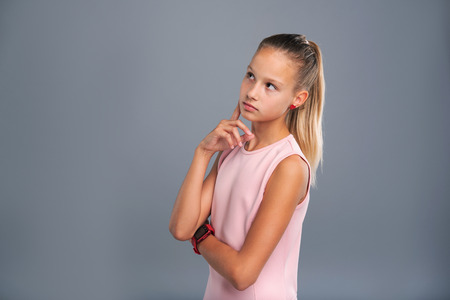 Fresh ideas. Petite teenage girl in a pink top touching her cheek with a finger while contemplating something and considering new ideasの写真素材
