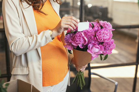 Pleasant gesture. Close up of tender female hands taking out present card from bouquet wrapped in paperの写真素材