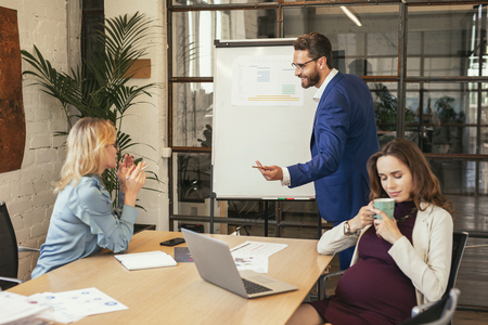 Business meeting. Calm female colleagues sitting at table and man standing near whiteboardの写真素材