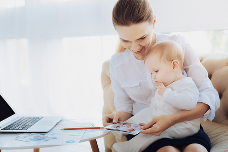 Look here. Charming young woman bowing head while showing photos to her babyの写真素材