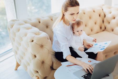 Modern technology. Attentive female person keeping diagram in left hand while staring at computerの写真素材