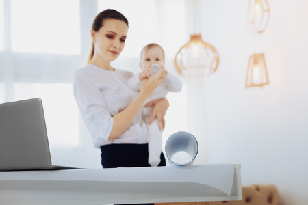 Good girl. Charming baby holding bottle in both hands while spending time with mommyの写真素材