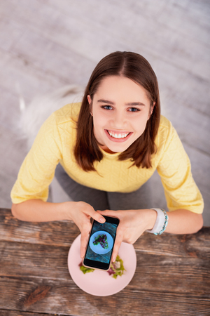 How to prepare. Top view of merry teen blogger using phone and looking at cameraの写真素材