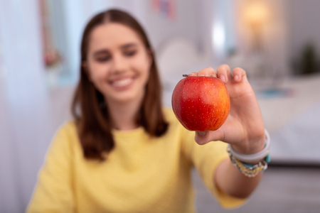 Juicy apple. Selective focus of fresh red apple hold by teen girl who smilingの写真素材