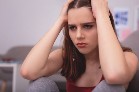 Emotional overwhelming. Depressed teen girl touching head and gazing straightの写真素材
