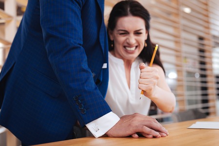 No touches. Resentful dark-haired woman hitting mans hand with a pencil while he caressing herの写真素材