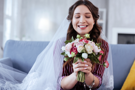 Wedding bouquet. Charming bride smiling broadly while holding nice wedding bouquet in her handsの写真素材
