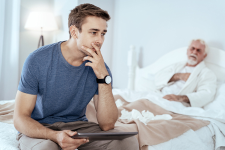 Buy online. Pensive man carrying tablet and senior man posing on bedの写真素材