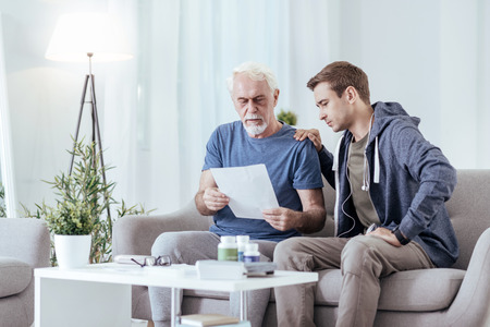 What to buy. Low angle of attentive senior man demonstrating paper to man and sitting on couchの写真素材