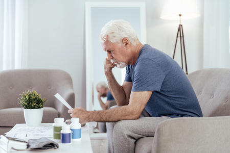 Concerning news. Thoughtful senior man posing in profile and studying paperの写真素材