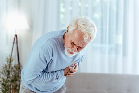 Coronary artery disease. Sick senior man touching chest and posing on light background