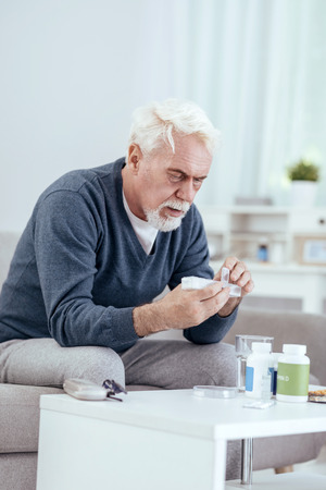 Medicative interference. Serious senior man sitting on sofa and taking pillsの写真素材