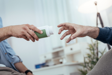 Saving medication. Close up of tensed male hand stretching for bottle filled with pillsの写真素材