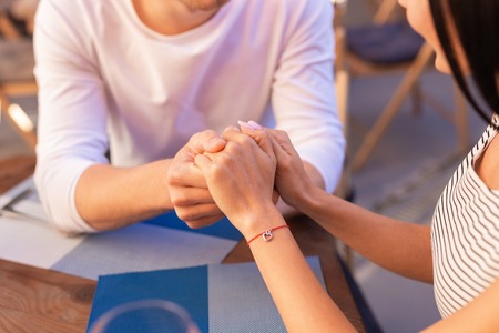Beautiful dark-haired woman wearing nice bracelet touching hands of her handsome manの写真素材