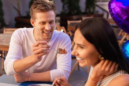 Offering dessert. Smiling businessman offering some dessert his young wife while spending summer evening togetherの写真素材