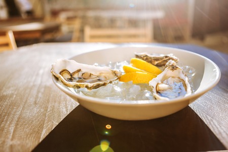 Lemon and oysters. Three thin pieces of lemon and three fresh delicious oysters lying on ice in plain white plateの写真素材