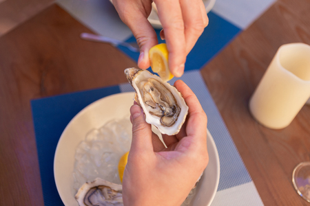 Mature prosperous man sprinkling some lemon juice on fresh oysters while relaxing on summer terraceの写真素材