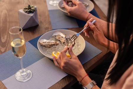 Dark-haired woman wearing nice wrist watch feeing rested while eating fresh delicious seafoodの写真素材