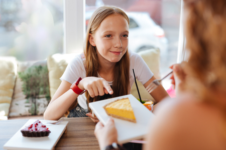 Blonde-haired pleasant schoolgirl eating delicious desserts with caring motherの写真素材