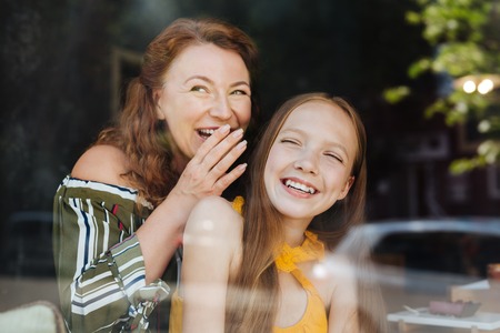 Red-haired beaming woman laughing out loud while standing with her daughter