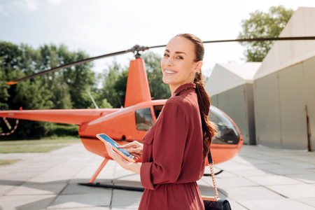 Cheerful pretty woman looking at camera and standing near helicopterの写真素材