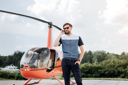 Satisfied enthusiastic man talking on phone and waiting near helicopterの写真素材
