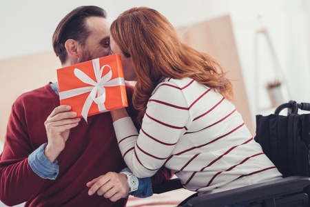 Emotional kiss. Adorable loving couple hiding behind a beautiful present and feeling happy while kissingの写真素材