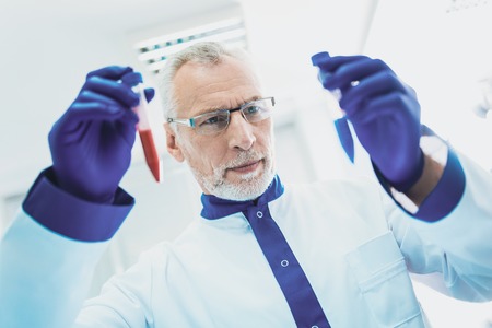 Attentive male person wrinkling forehead while looking at glass tubes