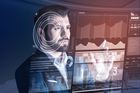 Calm and thoughtful. Clever young programmer frowning and looking attentively at the information on the transparent screen in front of himの写真素材