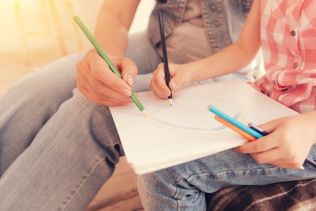New masterpiece is in progress. Scaled up look on a piece of paper lying on knees on a little girl drawing together with her granny while both spending leisure time together.の写真素材