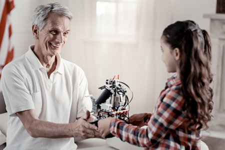 Proud girl captivated grandfather awarding girl for good notes with toy while she standing back to the cameraの写真素材
