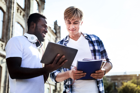 Project presentation. Cheerful international student keeping smile on his face and demonstrating his tablet while standing in semi positionの写真素材