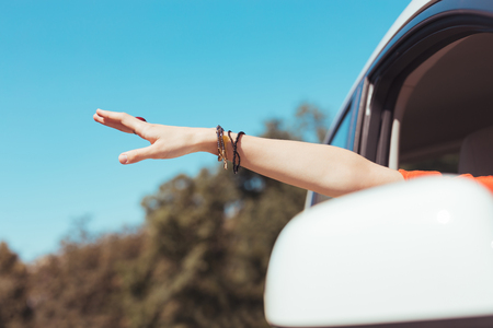 Woman wearing orange dress and accessories taking hand out of window during her travelの写真素材