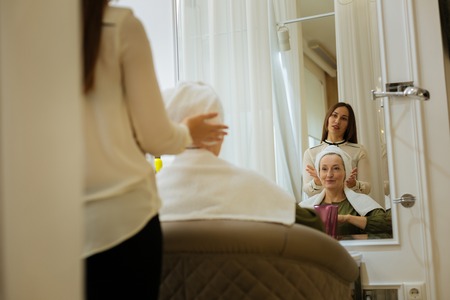 Joyful aged woman smiling while looking at herself in the mirrorの写真素材