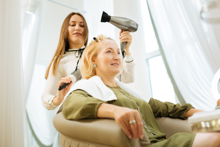 Joyful positive woman sitting in the chair while waiting for the hairstyle to be doneの写真素材