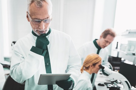 Thoughtful chemist. Professional chemist wearing glasses feeling rather thoughtful while enjoying making discovery at workの写真素材
