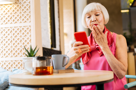 Joyful happy woman sending a kiss while having a video call on her smartphoneの写真素材