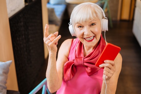 Happy aged woman holding her smartphone while listening to rock musicの写真素材