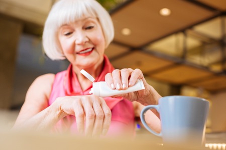 Cheerful senior woman using hand cream while caring about her skin